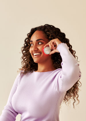 Woman using the OmniLux Blemish Eraser on her cheek with a beige background
