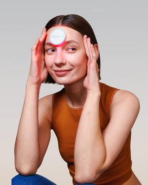 Woman using the OmniLux Blemish Eraser on her forhead against a plain background