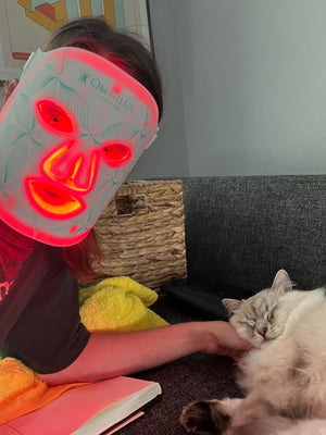 Person with a glowing mask petting a cat on a couch